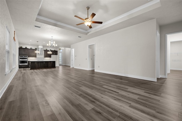 unfurnished living room featuring dark wood-style flooring, visible vents, ceiling fan with notable chandelier, and a raised ceiling