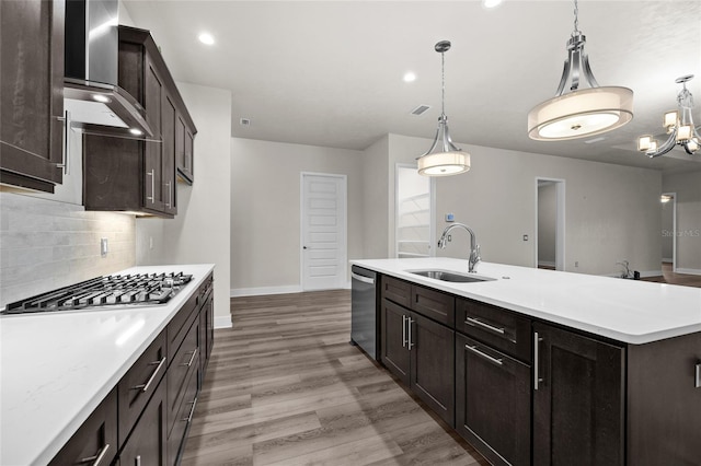 kitchen featuring light countertops, a sink, wall chimney exhaust hood, wood finished floors, and stainless steel appliances