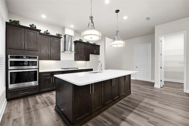 kitchen featuring visible vents, stainless steel double oven, a sink, light wood-style floors, and wall chimney range hood