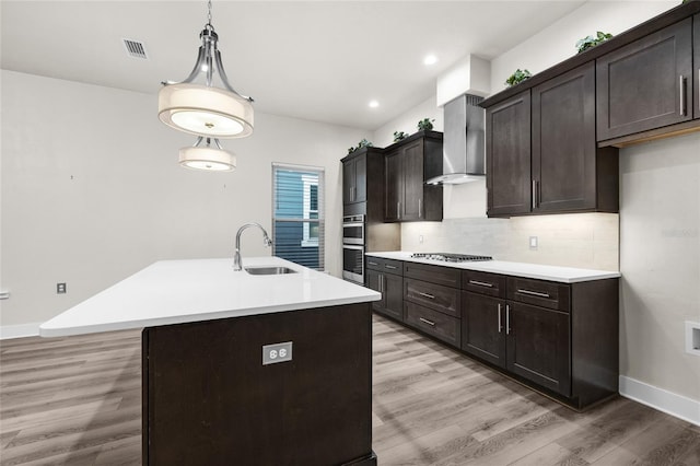 kitchen with stainless steel appliances, tasteful backsplash, a sink, light wood-style floors, and wall chimney range hood