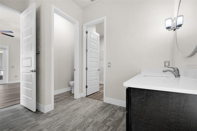 bathroom with baseboards, ceiling fan, toilet, and vanity