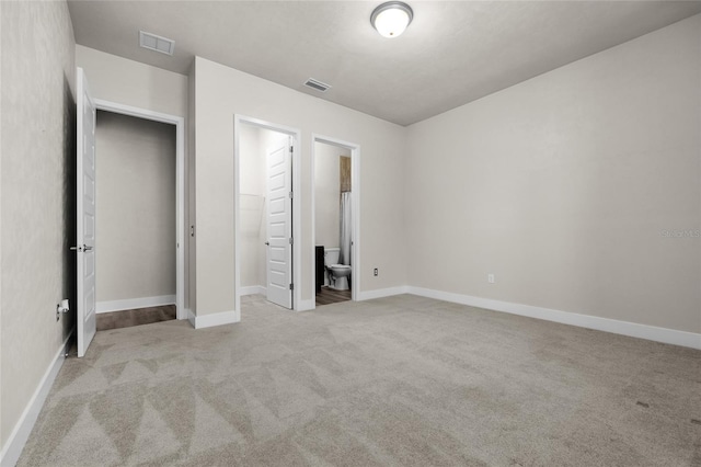 unfurnished bedroom featuring baseboards, ensuite bath, visible vents, and carpet