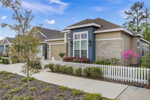 view of front of property with stone siding, an attached garage, concrete driveway, a fenced front yard, and a shingled roof