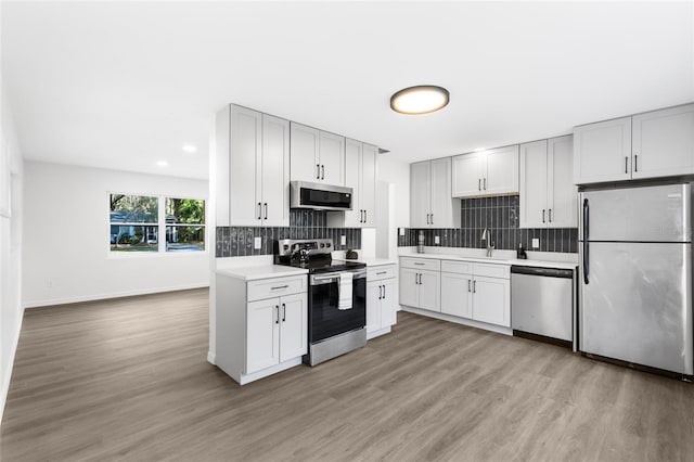 kitchen with decorative backsplash, light countertops, light wood finished floors, stainless steel appliances, and a sink