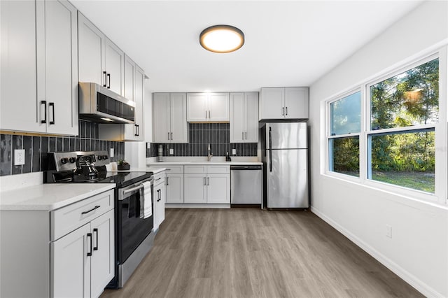 kitchen featuring stainless steel appliances, baseboards, decorative backsplash, a sink, and light wood-style floors