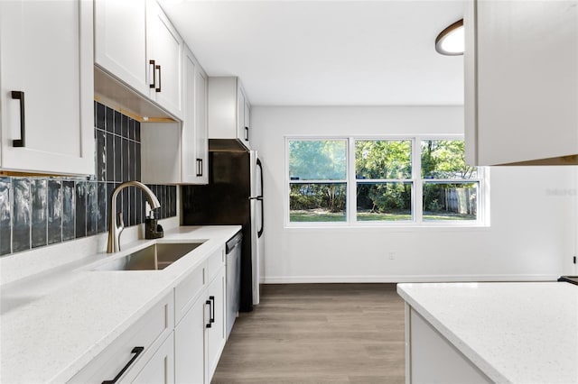 kitchen featuring a sink, white cabinetry, light stone countertops, stainless steel dishwasher, and light wood-style floors