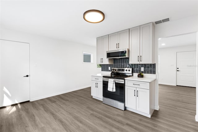 kitchen with light countertops, light wood-style floors, decorative backsplash, and appliances with stainless steel finishes