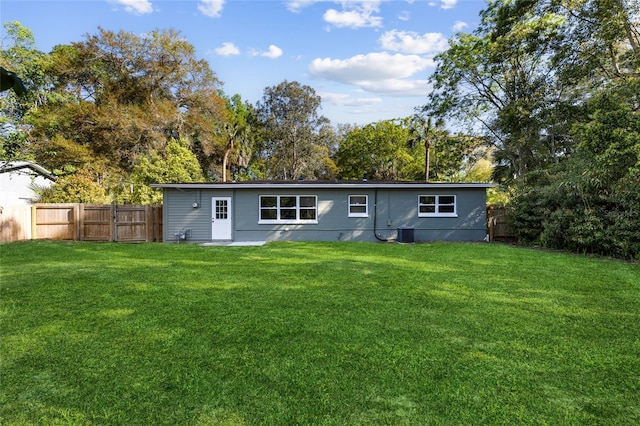 rear view of house with central air condition unit, a lawn, and fence