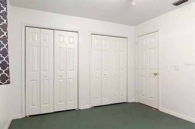 unfurnished bedroom featuring baseboards, multiple closets, visible vents, and finished concrete flooring
