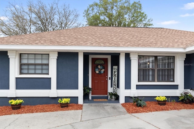 entrance to property with a shingled roof and stucco siding