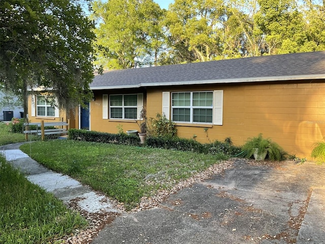 view of front of home with roof with shingles, a front yard, and concrete block siding