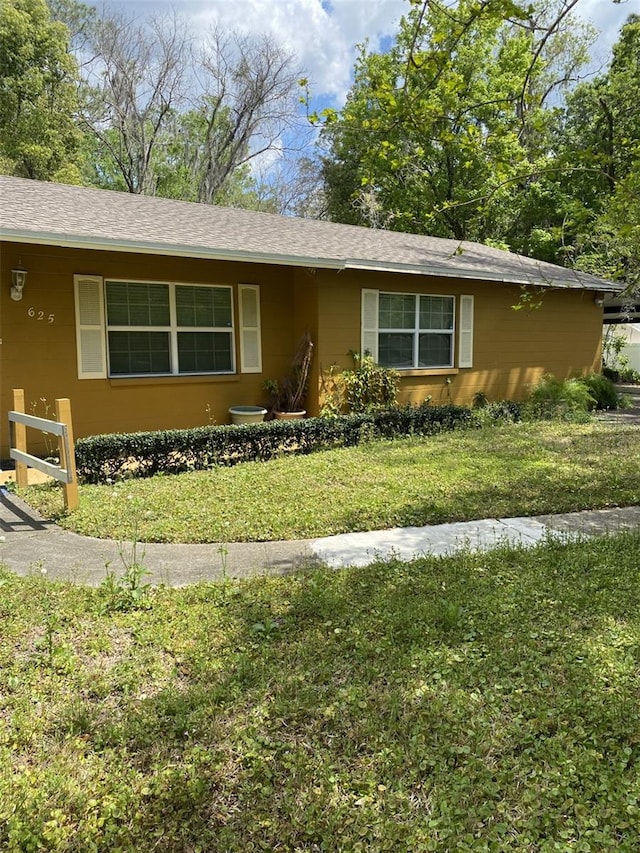 ranch-style house featuring a shingled roof and a front yard