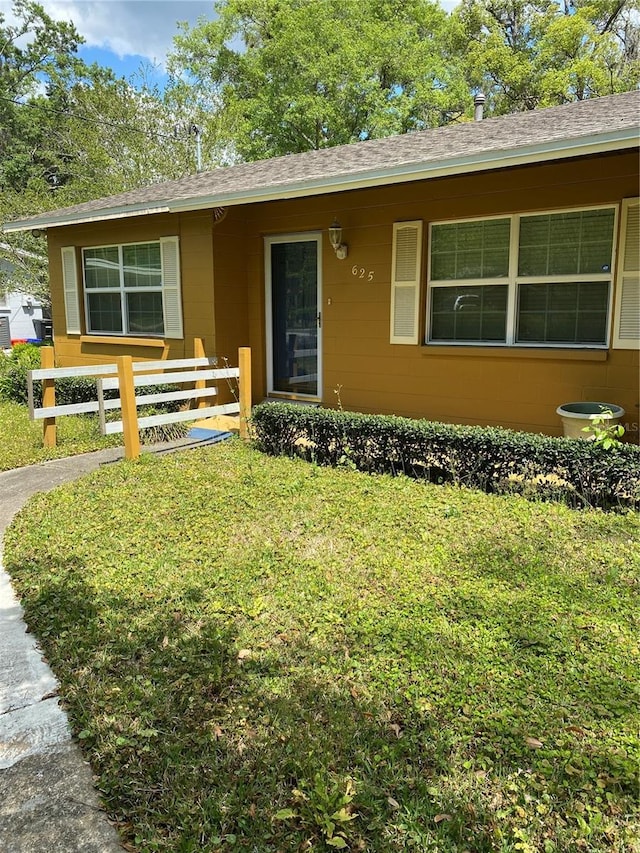 ranch-style home featuring fence, a shingled roof, and a front lawn