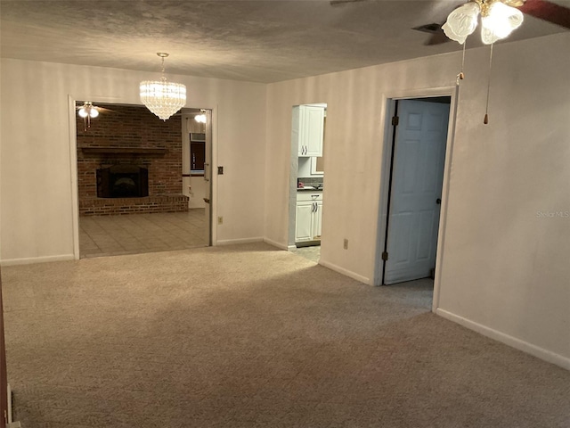 unfurnished room with baseboards, light carpet, a brick fireplace, and ceiling fan with notable chandelier