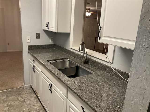 kitchen featuring white cabinets, dark stone countertops, light carpet, and a sink