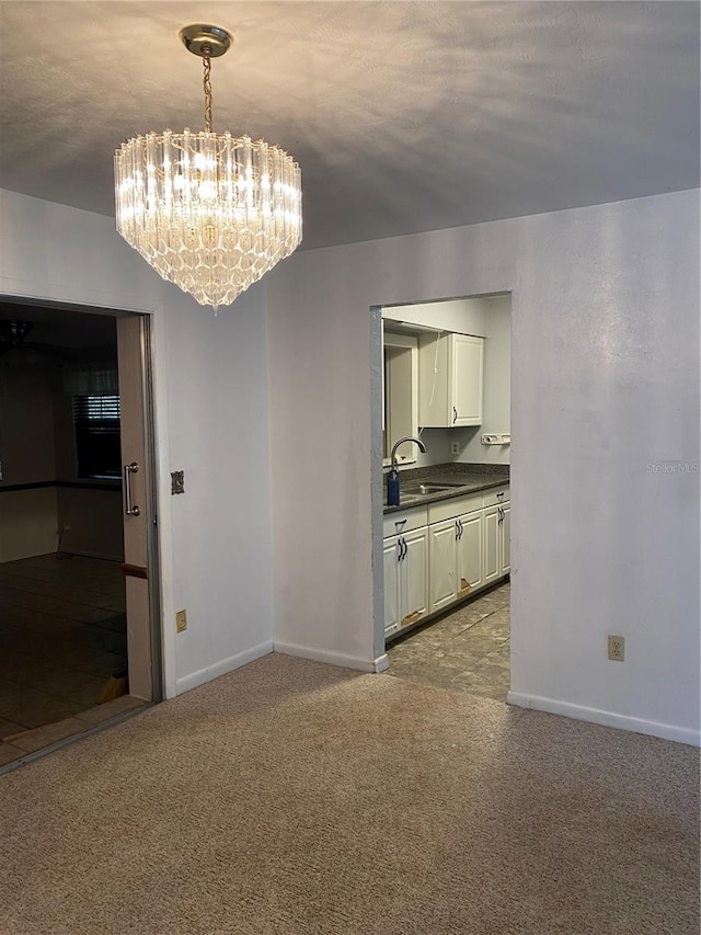 unfurnished dining area featuring a sink, carpet floors, baseboards, and a chandelier