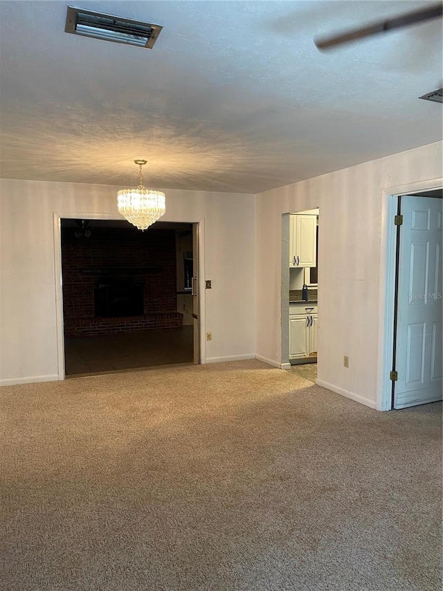 empty room featuring light colored carpet, baseboards, a brick fireplace, and a notable chandelier