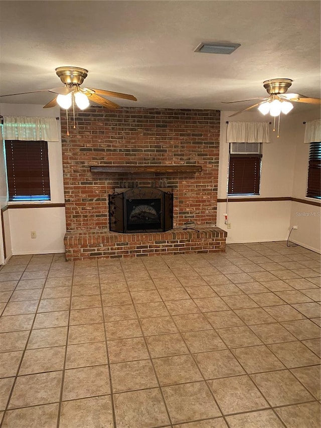 unfurnished living room with visible vents, ceiling fan, tile patterned flooring, a brick fireplace, and baseboards