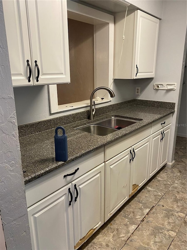 kitchen with a sink, white cabinetry, and dark stone countertops