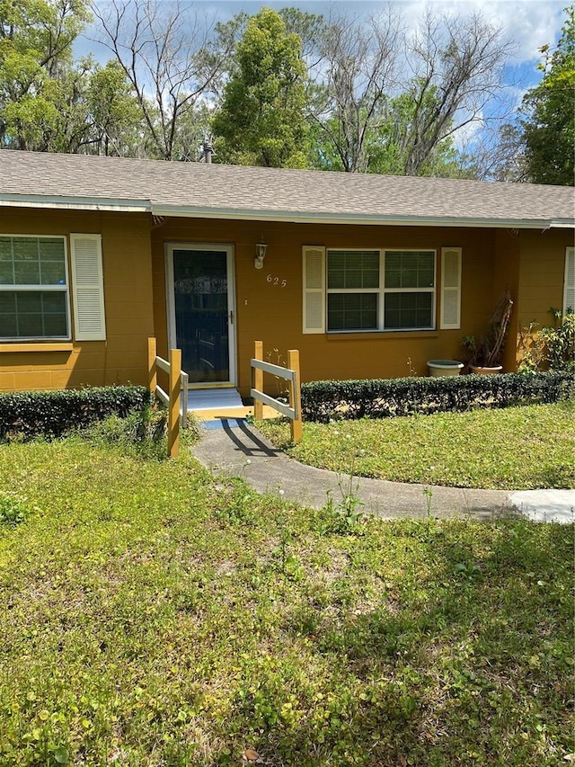single story home with a front lawn, roof with shingles, and concrete block siding