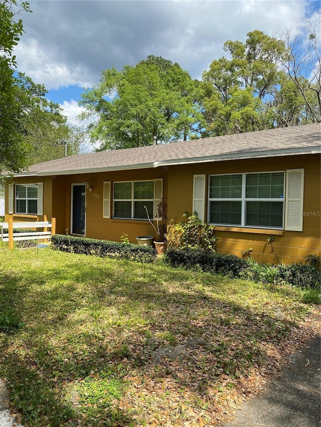 ranch-style house featuring a shingled roof and a front yard