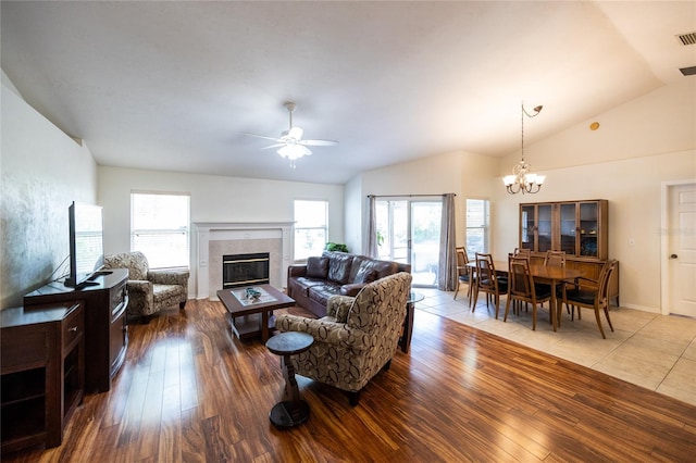 living area with plenty of natural light, a fireplace, vaulted ceiling, wood finished floors, and ceiling fan with notable chandelier