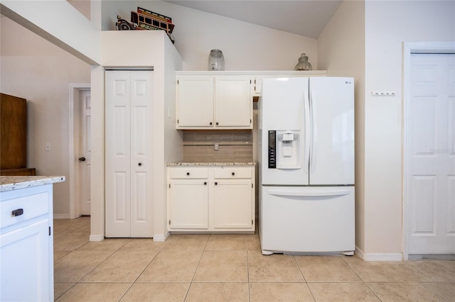 kitchen with light stone countertops, white refrigerator with ice dispenser, white cabinetry, light tile patterned floors, and lofted ceiling
