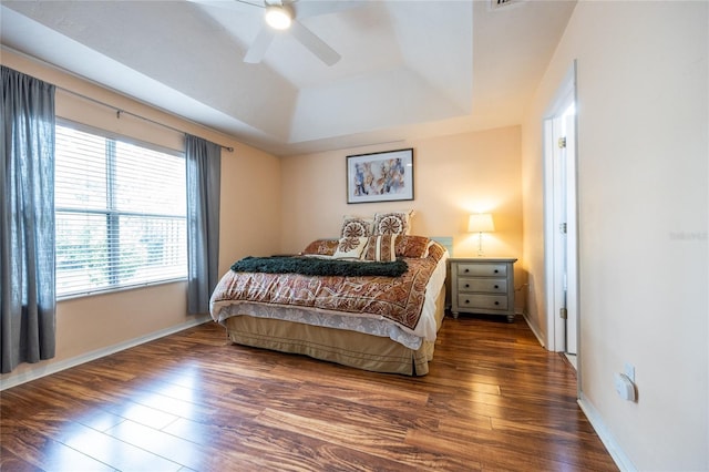bedroom with ceiling fan, a raised ceiling, baseboards, and wood finished floors