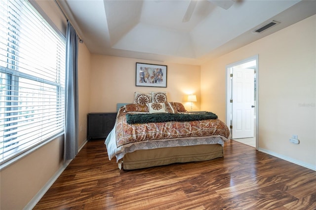 bedroom featuring visible vents, baseboards, wood finished floors, and a tray ceiling
