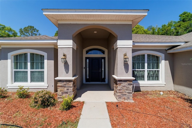 view of exterior entry with stucco siding, a shingled roof, and stone siding