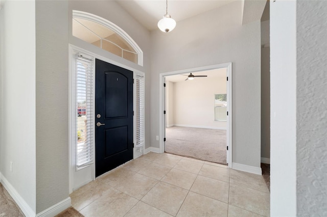foyer entrance with light carpet, baseboards, ceiling fan, and light tile patterned floors