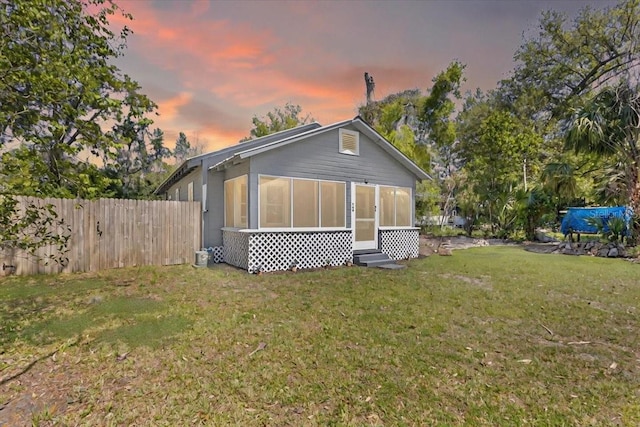 back of property featuring a lawn, a sunroom, and fence