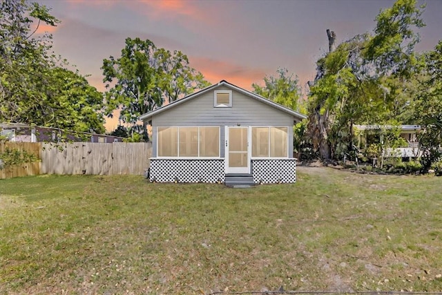 back of property at dusk featuring a sunroom, fence, and a yard