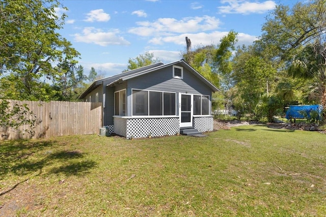 rear view of house with a lawn, a sunroom, and fence