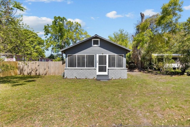 rear view of house featuring a lawn, a sunroom, and fence