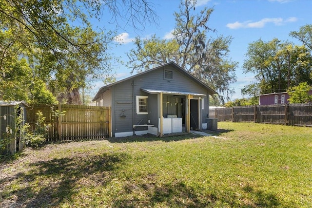rear view of property featuring cooling unit, a fenced backyard, an outbuilding, and a yard