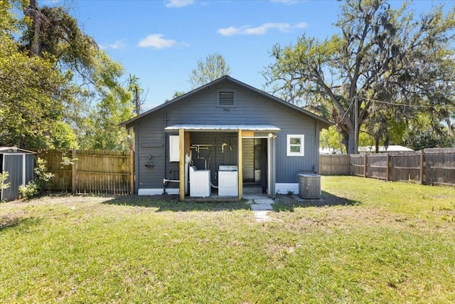 back of property featuring a fenced backyard, an outbuilding, separate washer and dryer, and a lawn