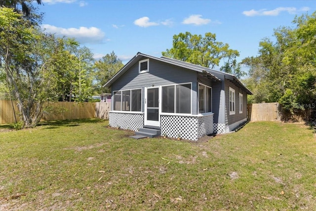 back of property with a fenced backyard, a lawn, and a sunroom