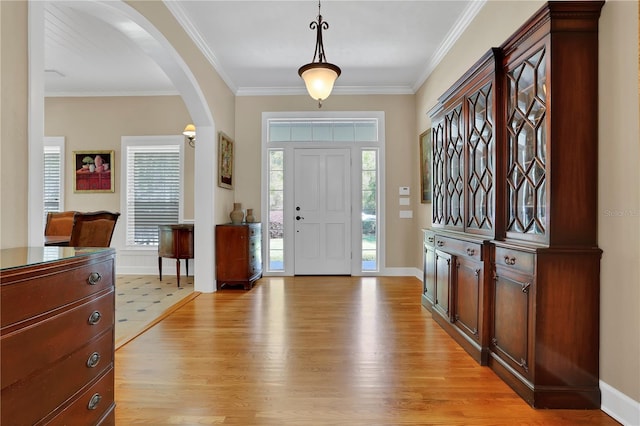 foyer featuring baseboards, crown molding, arched walkways, and light wood-style floors