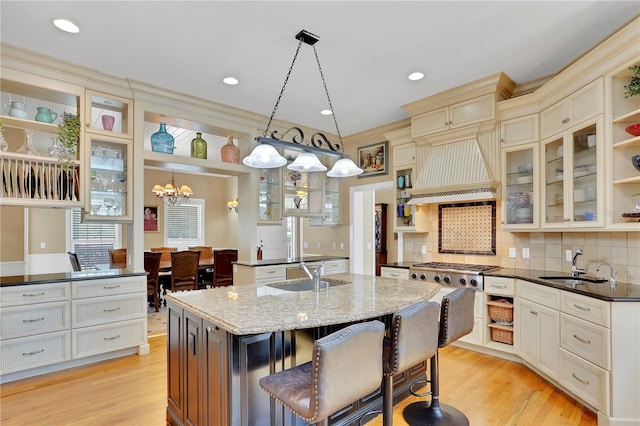 kitchen with light wood-style flooring, custom exhaust hood, a center island with sink, a sink, and open shelves