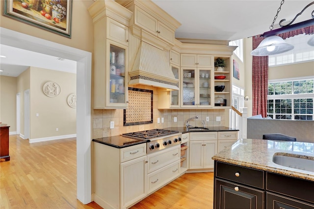 kitchen with backsplash, stainless steel gas cooktop, custom exhaust hood, and a sink