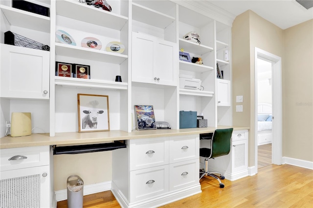 home office with baseboards, light wood-type flooring, built in desk, and visible vents