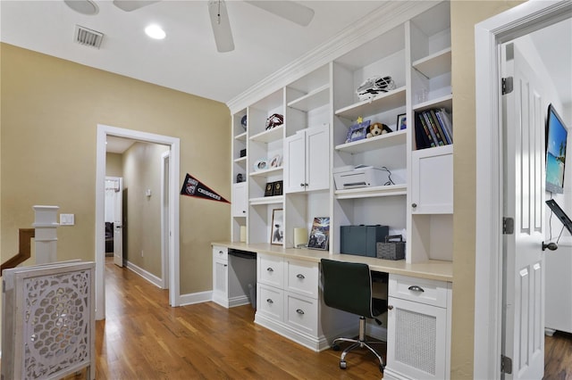 home office with built in study area, dark wood-style floors, baseboards, visible vents, and ceiling fan