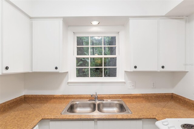 kitchen with a sink, white cabinets, range, and light countertops
