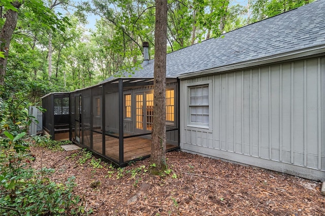 view of side of home featuring a shingled roof, a sunroom, board and batten siding, and a chimney