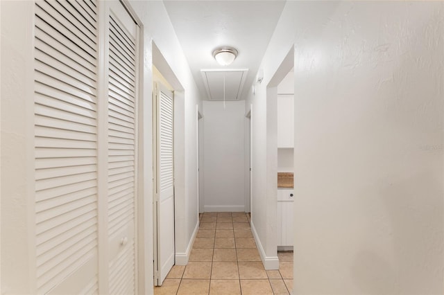 corridor featuring attic access, light tile patterned flooring, and baseboards