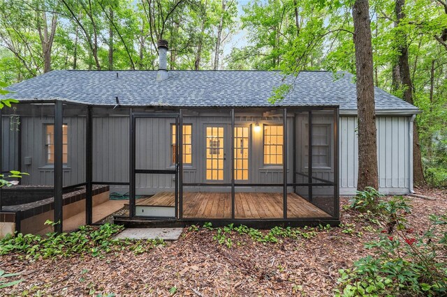 rear view of house with roof with shingles, a sunroom, and a deck