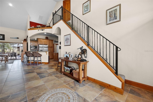 staircase with arched walkways, high vaulted ceiling, baseboards, and visible vents