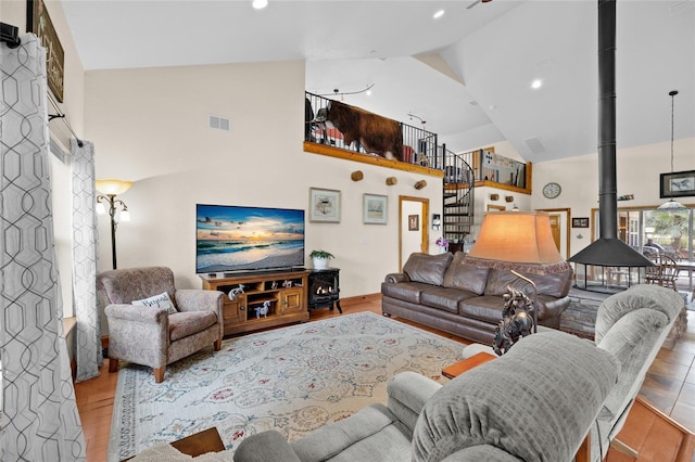 living area with stairway, recessed lighting, a wood stove, high vaulted ceiling, and wood finished floors