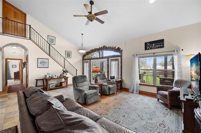 living area with high vaulted ceiling, stairway, baseboards, arched walkways, and ceiling fan